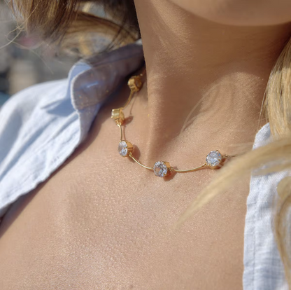 Close-up of a gold necklace with floral design on a person wearing a white top.