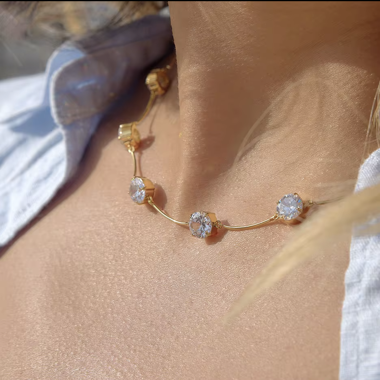 Gold necklace with gemstones on a person's wrist against a blurred natural background