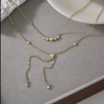 gold double layered necklace with clear gemstones pictured on a grey background
