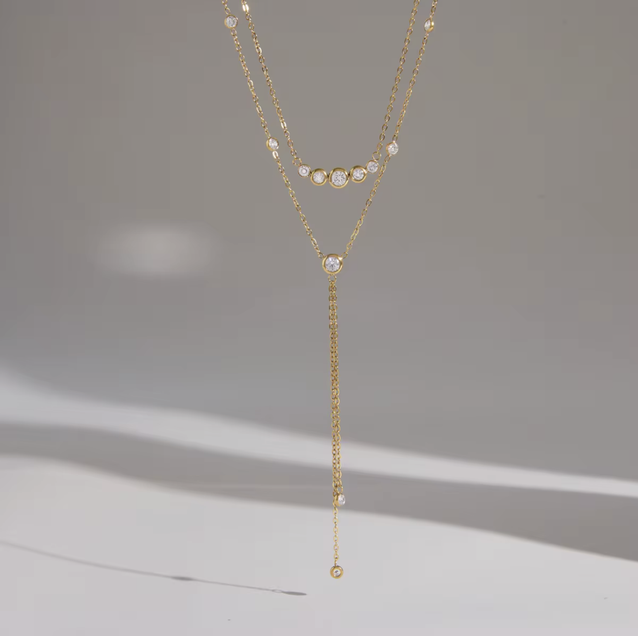 gold double layered necklace with clear gemstones pictured on a grey background