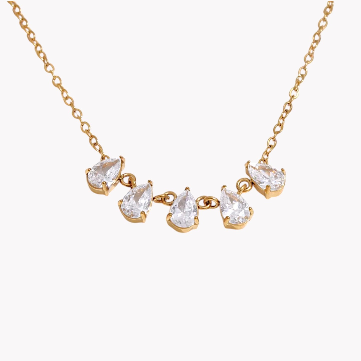 gold necklace featuring a row of 5 small pear shaped gemstones pictured on a light grey background