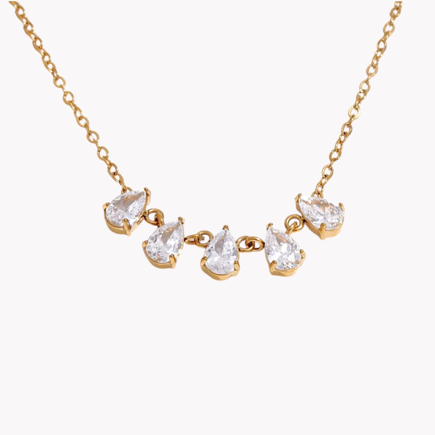 gold necklace featuring a row of 5 small pear shaped gemstones pictured on a light grey background