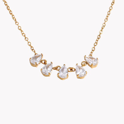 gold necklace featuring a row of 5 small pear shaped gemstones pictured on a light grey background