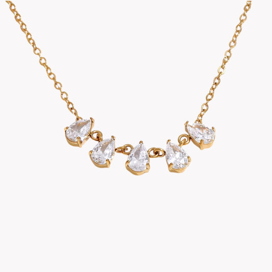 gold necklace featuring a row of 5 small pear shaped gemstones pictured on a light grey background