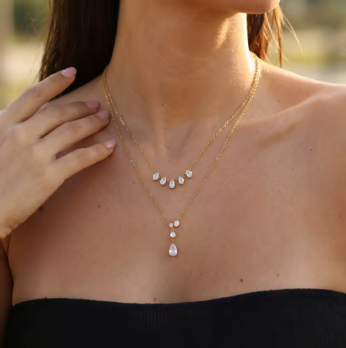 gold necklace featuring a row of 5 small pear shaped gemstones pictured being worn around the neck