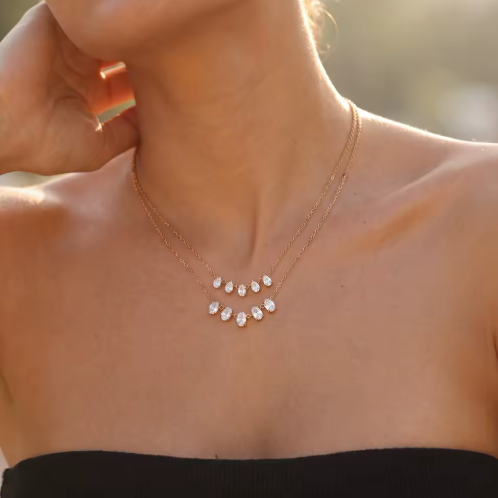 gold necklace featuring a row of 5 small pear shaped gemstones pictured being worn around the neck