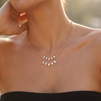 gold necklace featuring a row of 5 small pear shaped gemstones pictured being worn around the neck