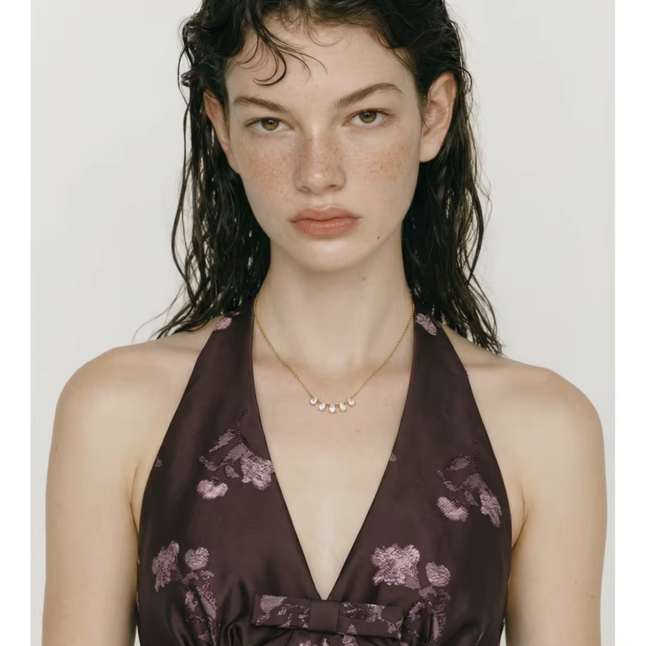 gold necklace featuring a row of 5 small pear shaped gemstones pictured being worn around the neck