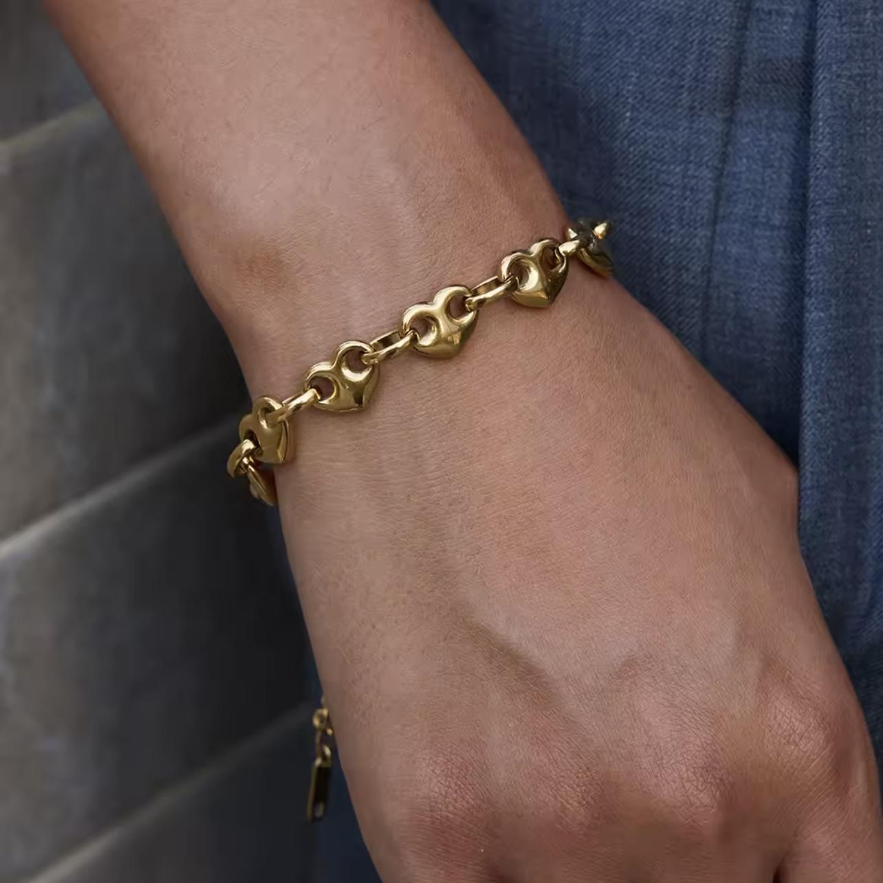 Gold chunky chain bracelet with heart chaped links being worn on a wrist