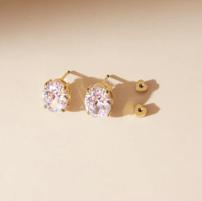 Gold earrings with clear gemstones on a beige background