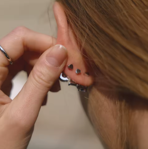Close-up of a person wearing small silver earrings with a neutral background
