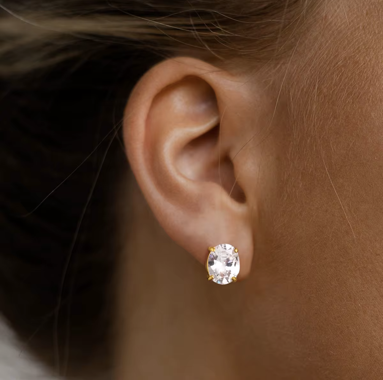 Close-up of an ear wearing a diamond stud earring with a blurred background