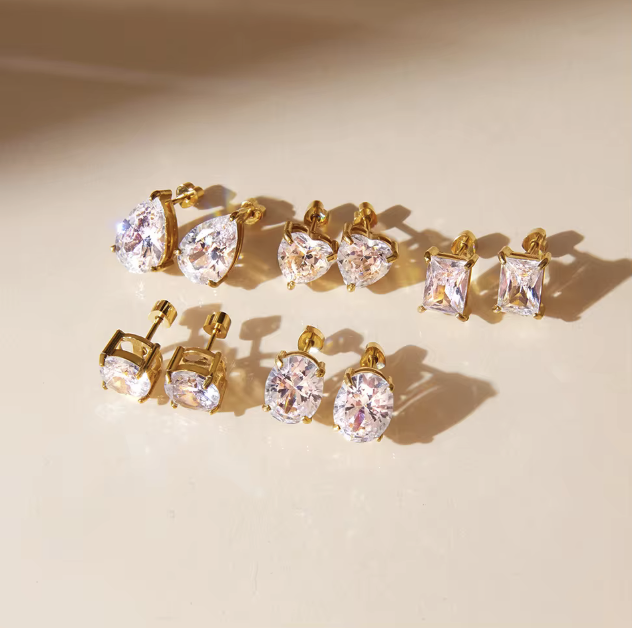 Set of gold and crystal earrings on a beige background