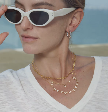 Woman wearing white sunglasses and gold necklaces with a blurred beach background