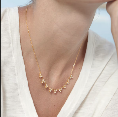 Gold necklace with heart-shaped pendants worn by a person in a white outfit.