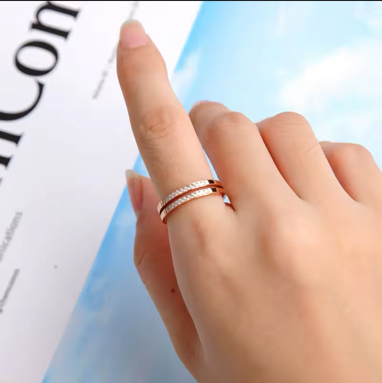 A gold-colored double layer ring with small embedded stones being worn on a finger