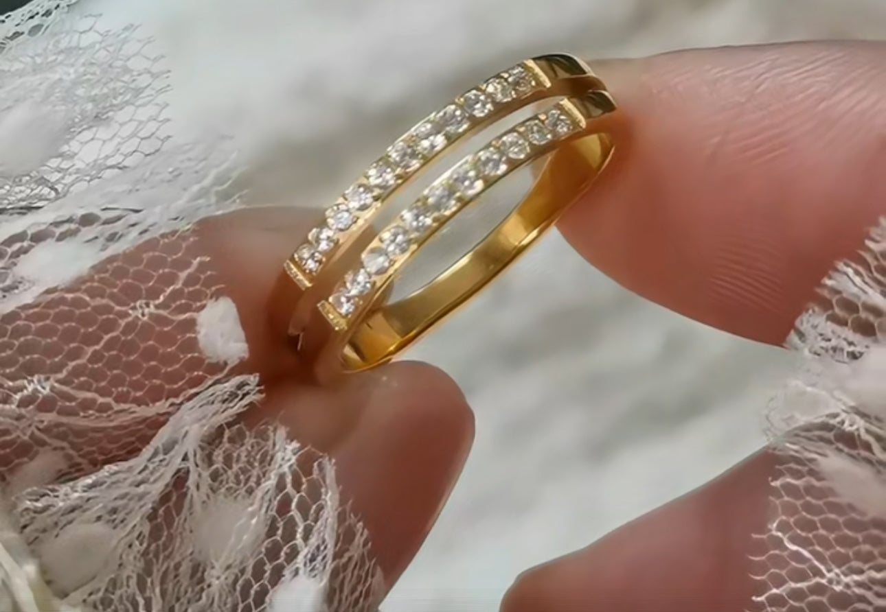 A gold-colored double layer ring with small embedded stones being worn on a finger