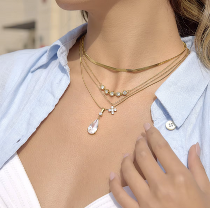 Person wearing a gold necklace with multiple pendants, set against a blurred background.