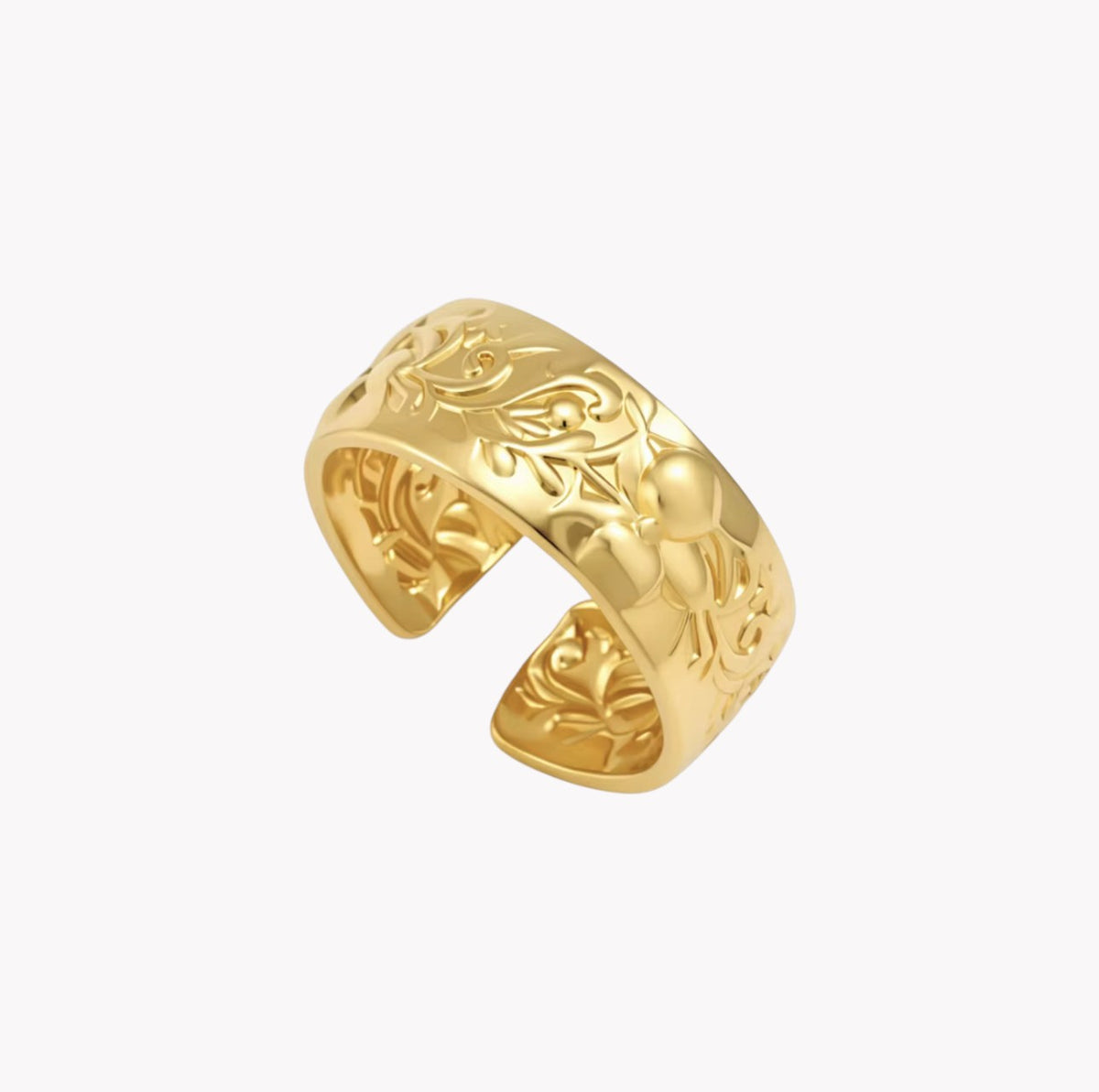 A wide gold-toned cuff ring with intricate floral and leaf engravings, shown on a plain light gray background.