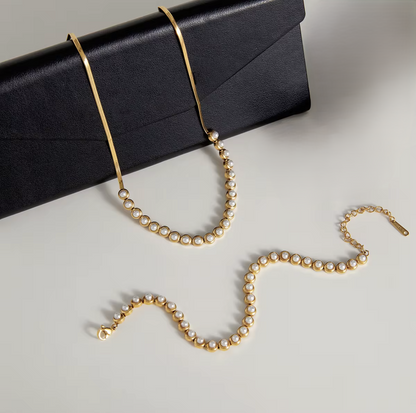 Gold necklace with pearls draped over a black box and a matching bracelet on a light gray surface