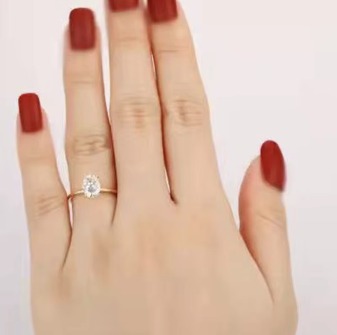 Hand wearing a gold ring with a oval cut diamond on a plain background