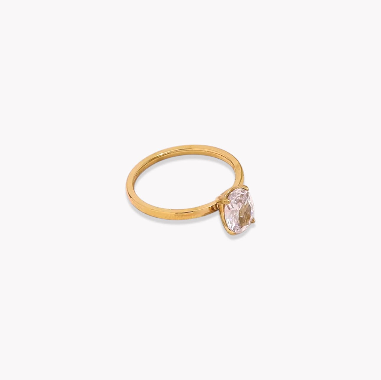 Gold ring with a clear oval cut gemstone on a white background