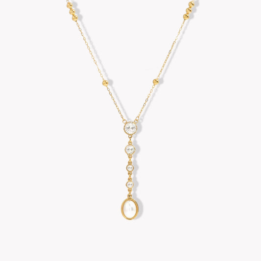 gold necklace with crystal and pearl detail pictured on a light grey background