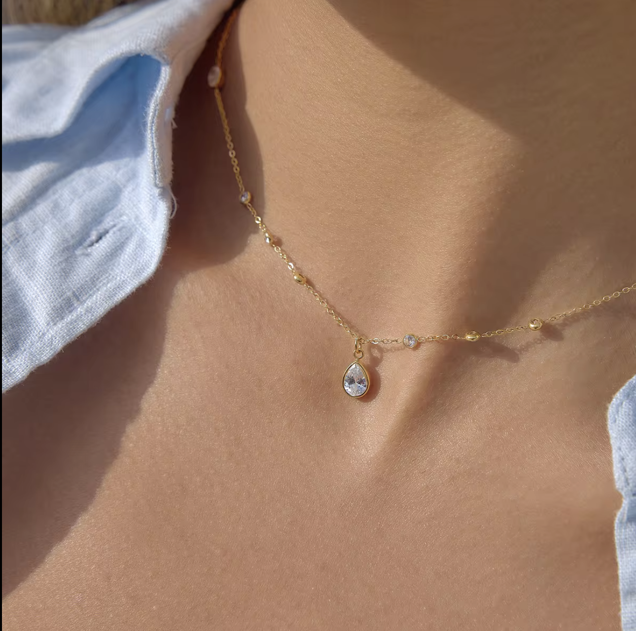 Gold necklace with a teardrop pendant on a person's neck