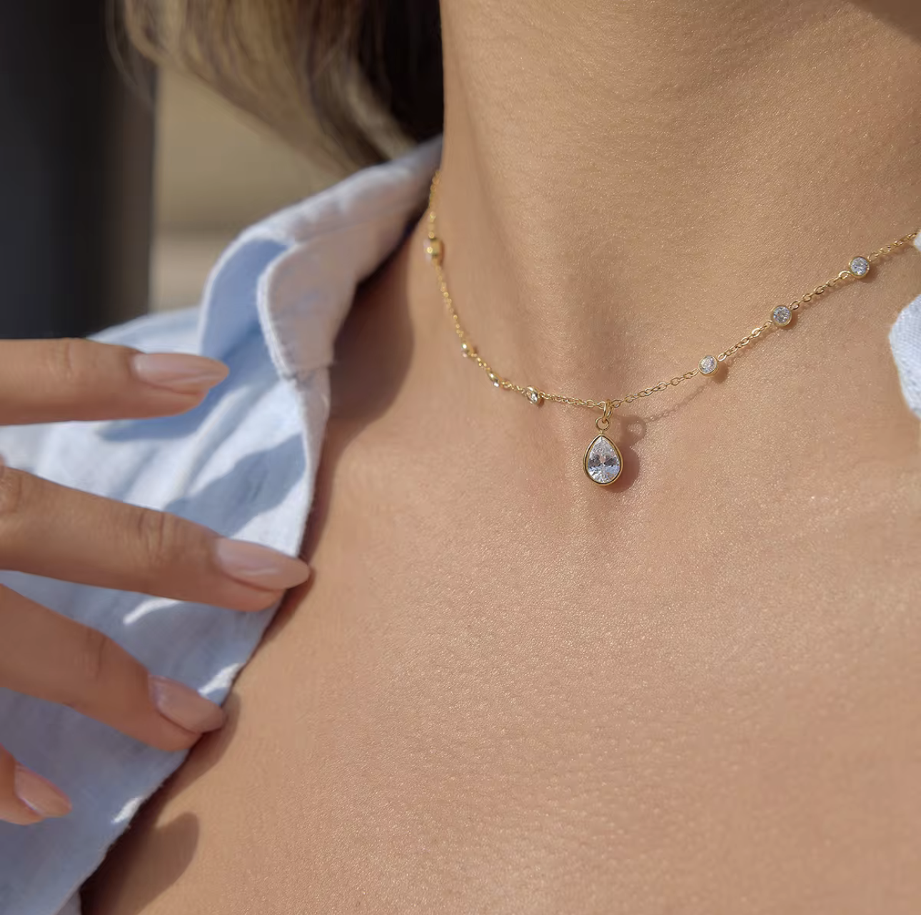 Gold necklace with a teardrop pendant worn by a person.
