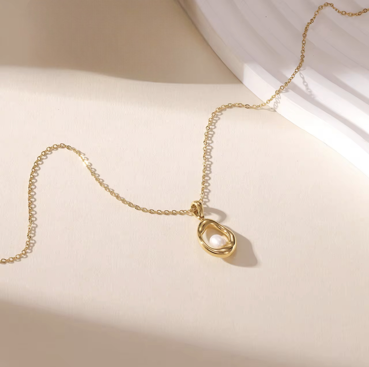 gold necklace with circular pendant featuring a small pearl inside pictured on a neutral background