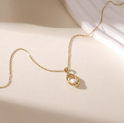 gold necklace with circular pendant featuring a small pearl inside pictured on a neutral background
