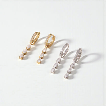 Two pairs of hoop earrings, one silver and one gold. Both with gemstone detail on the hoop and a 3 pear shaped clear gemstone drop detail. Pictured on a light grey background