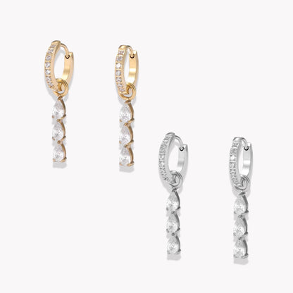 Two pairs of hoop earrings, one silver and one gold. Both with gemstone detail on the hoop and a 3 pear shaped clear gemstone drop detail. Pictured on a light grey background