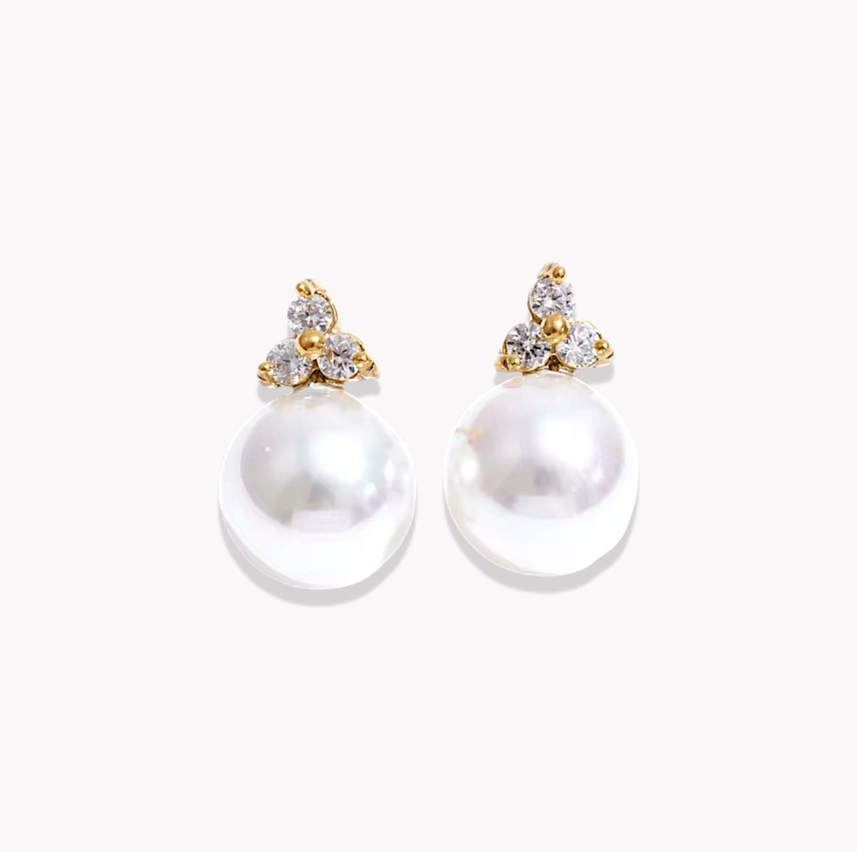A pair of gold and pearl stud earrings with clear gemstone accents, displayed on a clean white background.
