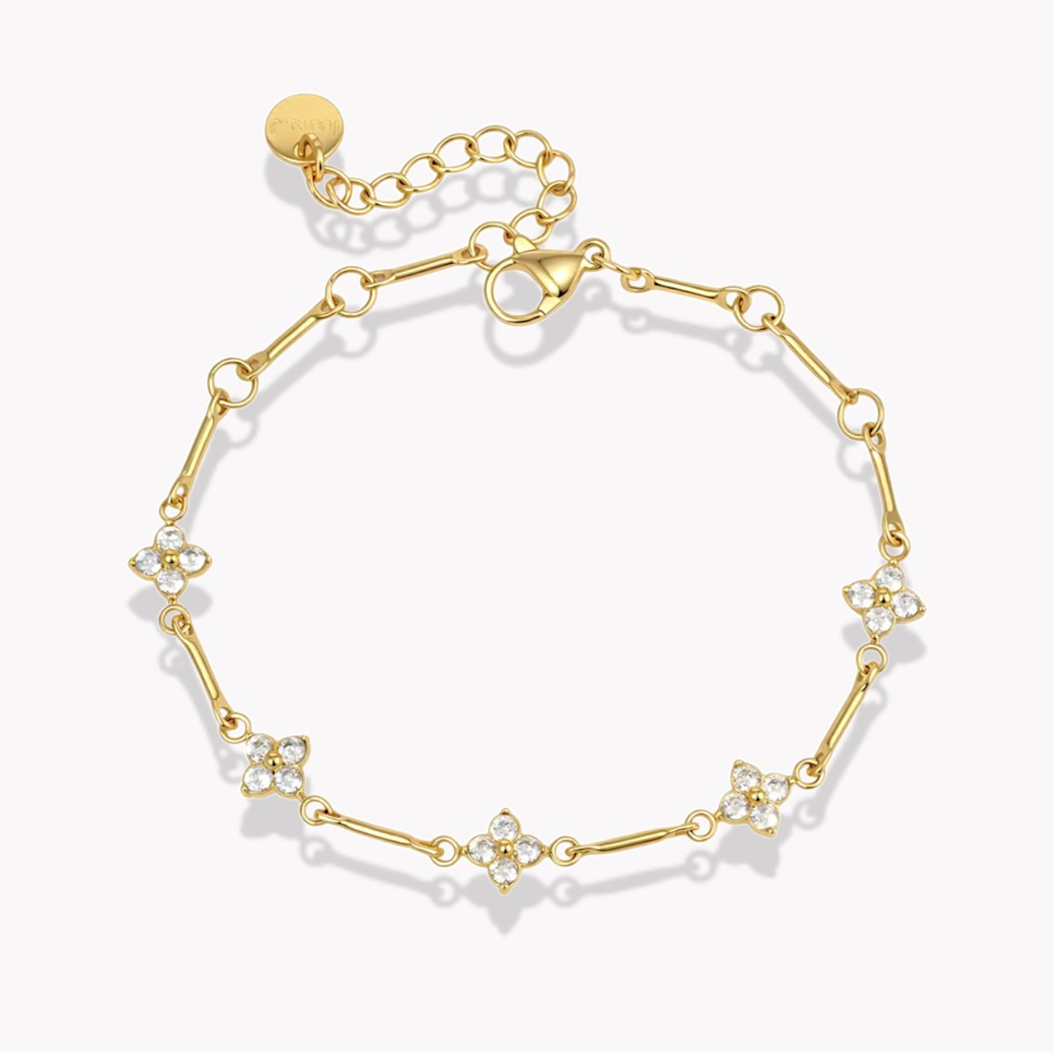 gold bracelet with small flower shaped gemstones pictured on a light grey background