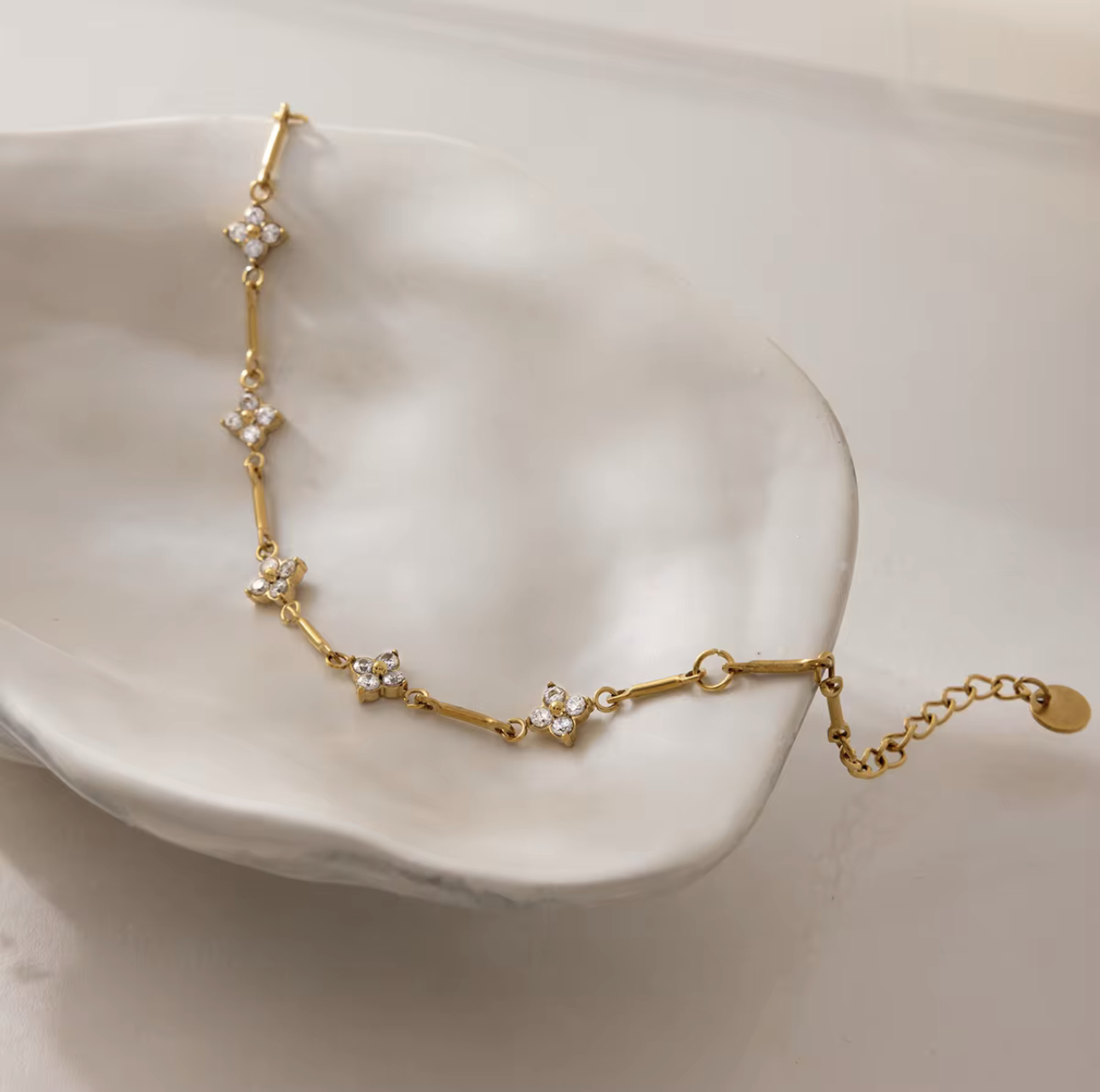 gold bracelet with small flower shaped gemstones pictured on a light coloured dish