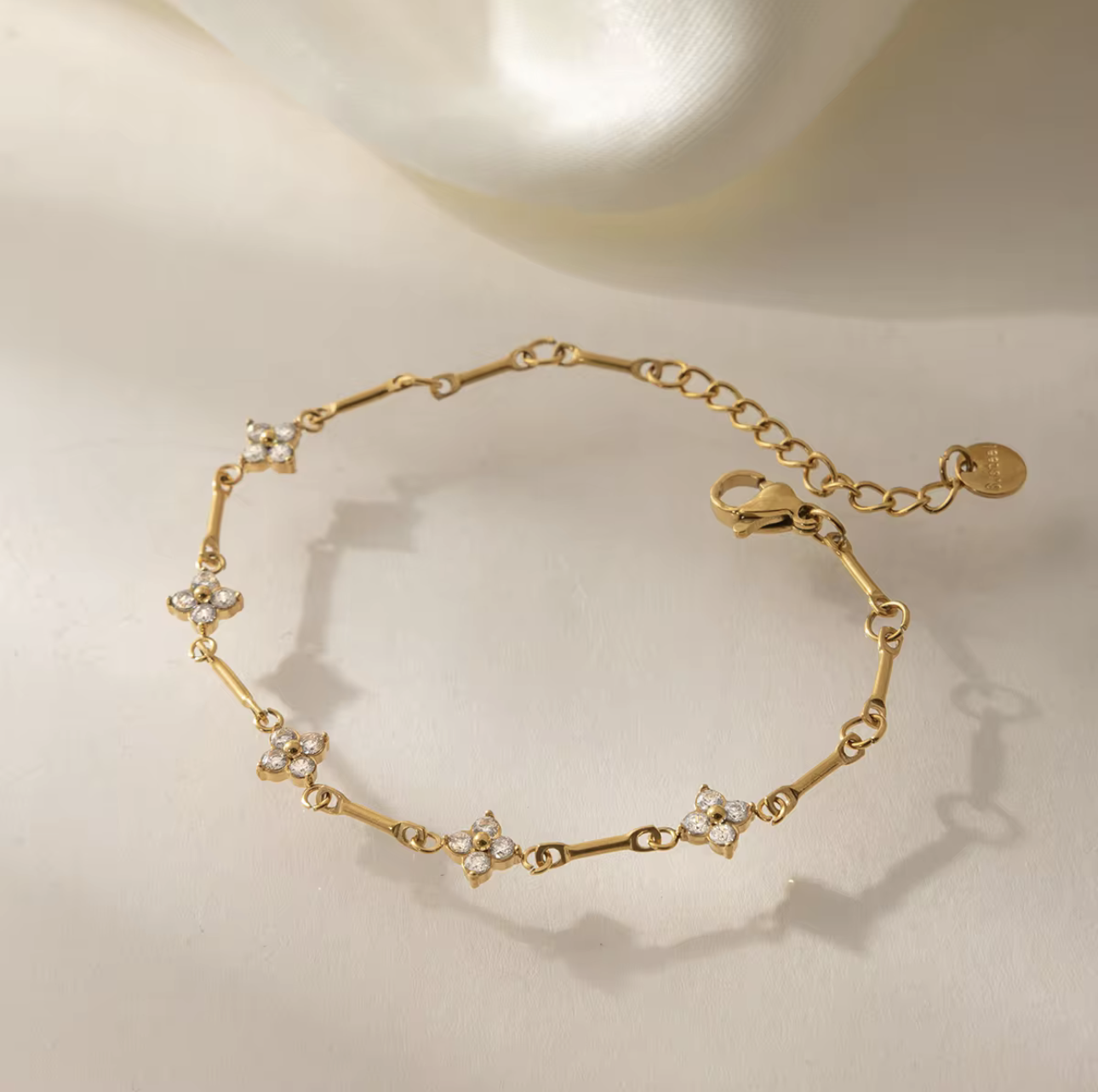 gold bracelet with small flower shaped gemstones pictured on a light background