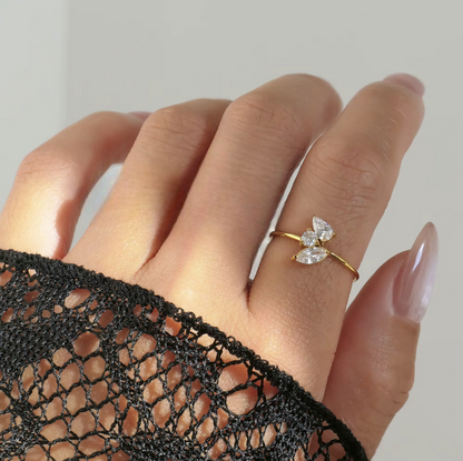 Hand wearing a gold ring with a clear gemstone against a neutral background