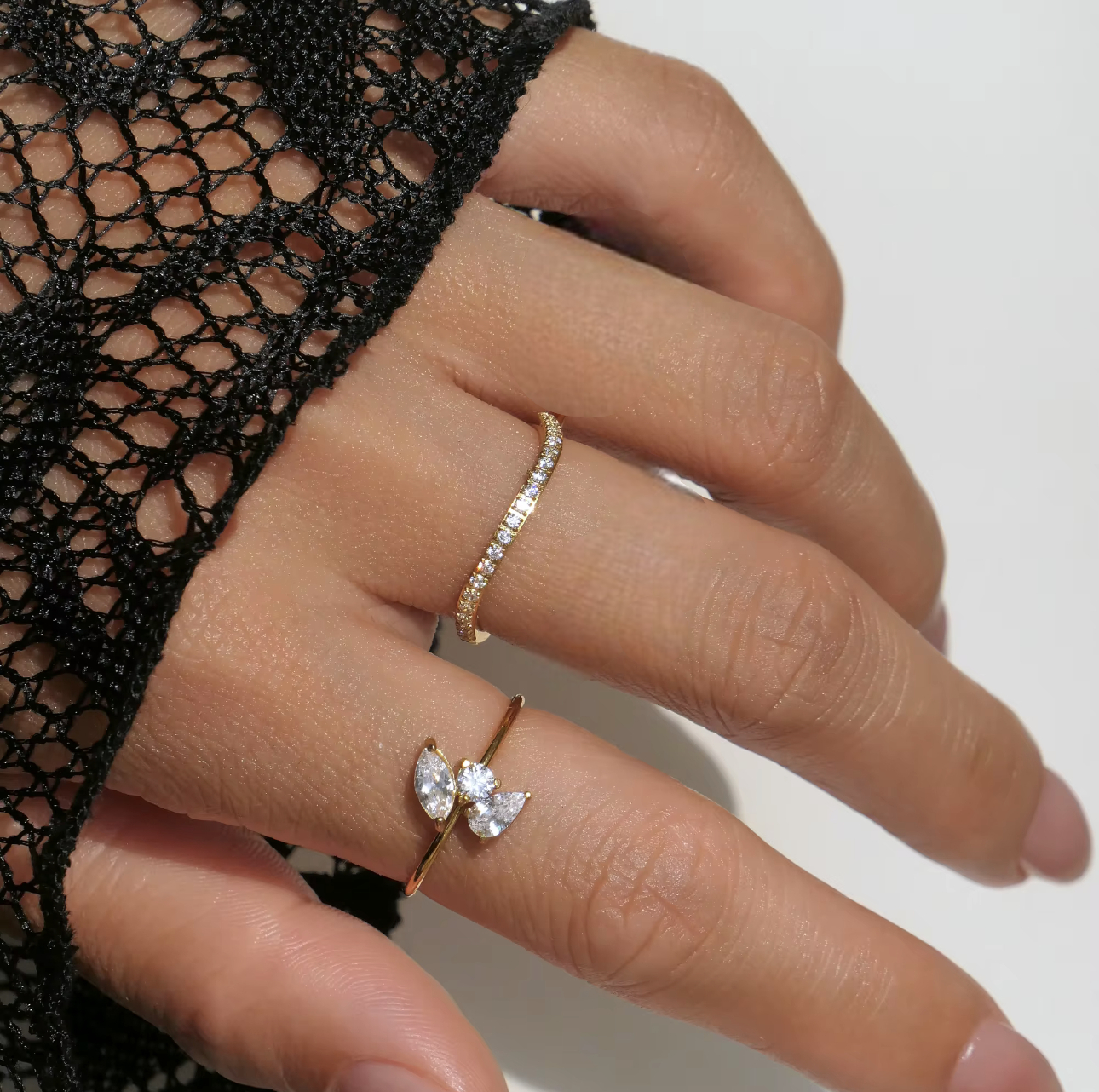 Close-up of a hand wearing two diamond rings on a neutral background