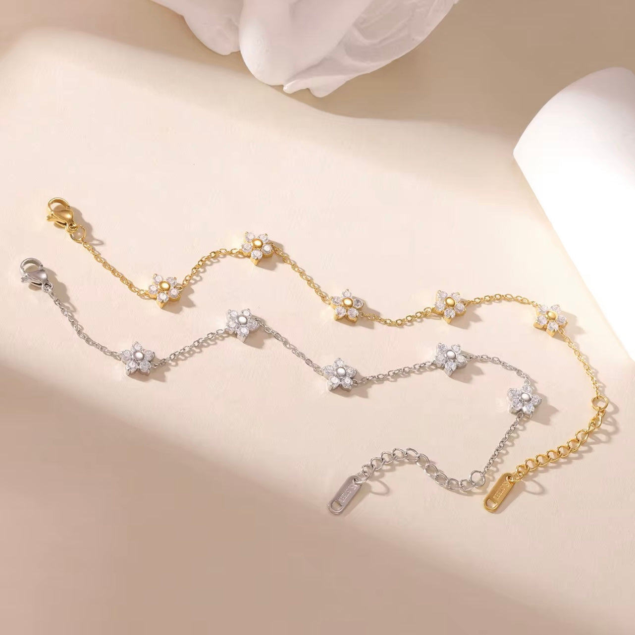 Gold and silver bracelets with clear gemstone floral design on a beige background