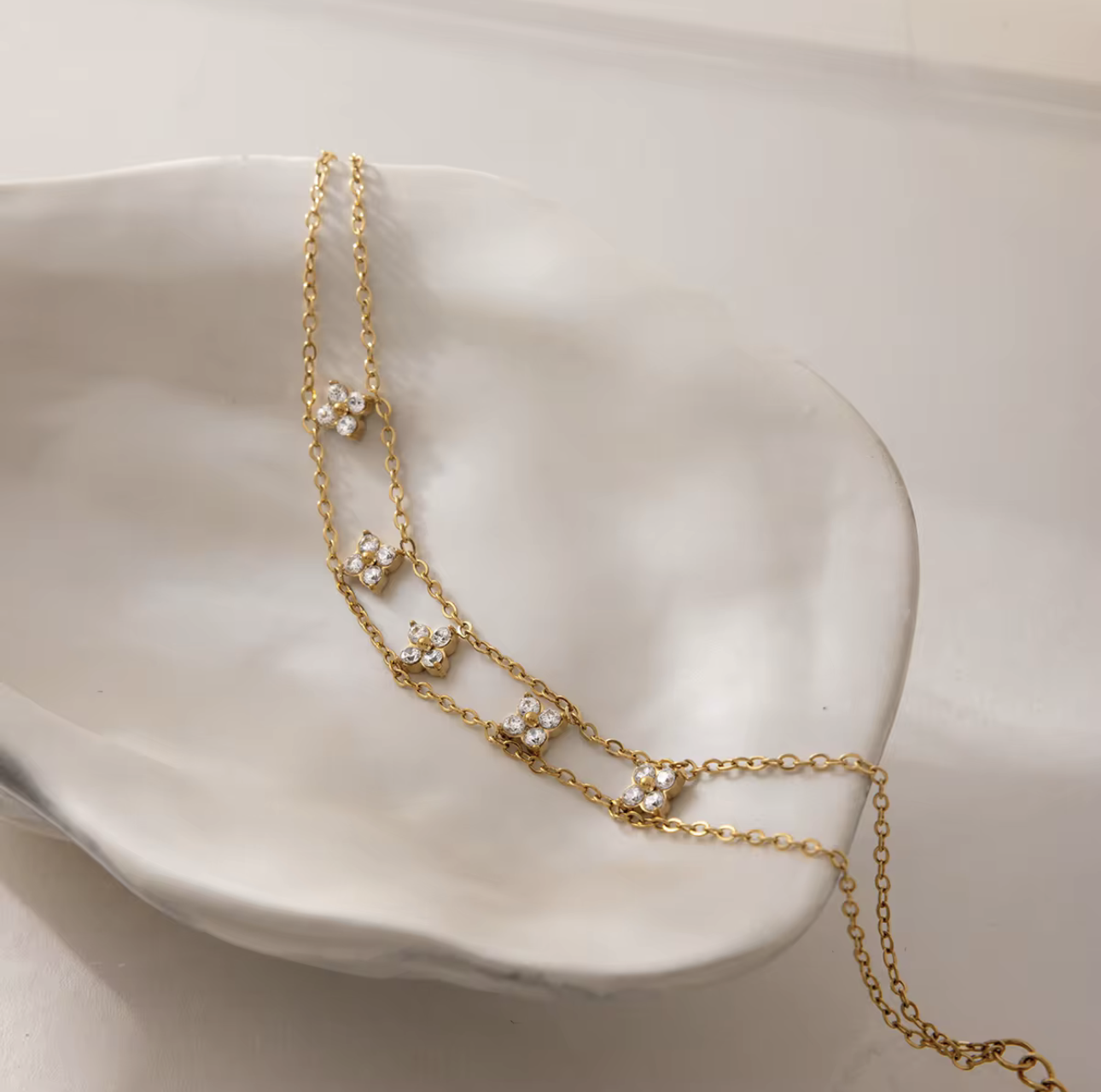 Gold chain necklace with floral pendants on a white ceramic dish
