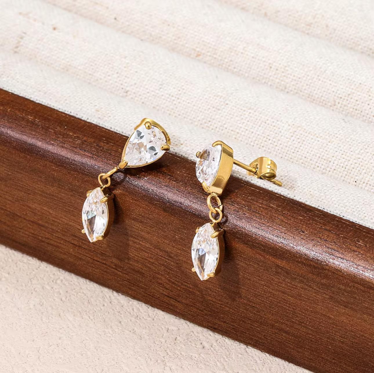 Gold earrings with clear gemstones on a wooden surface