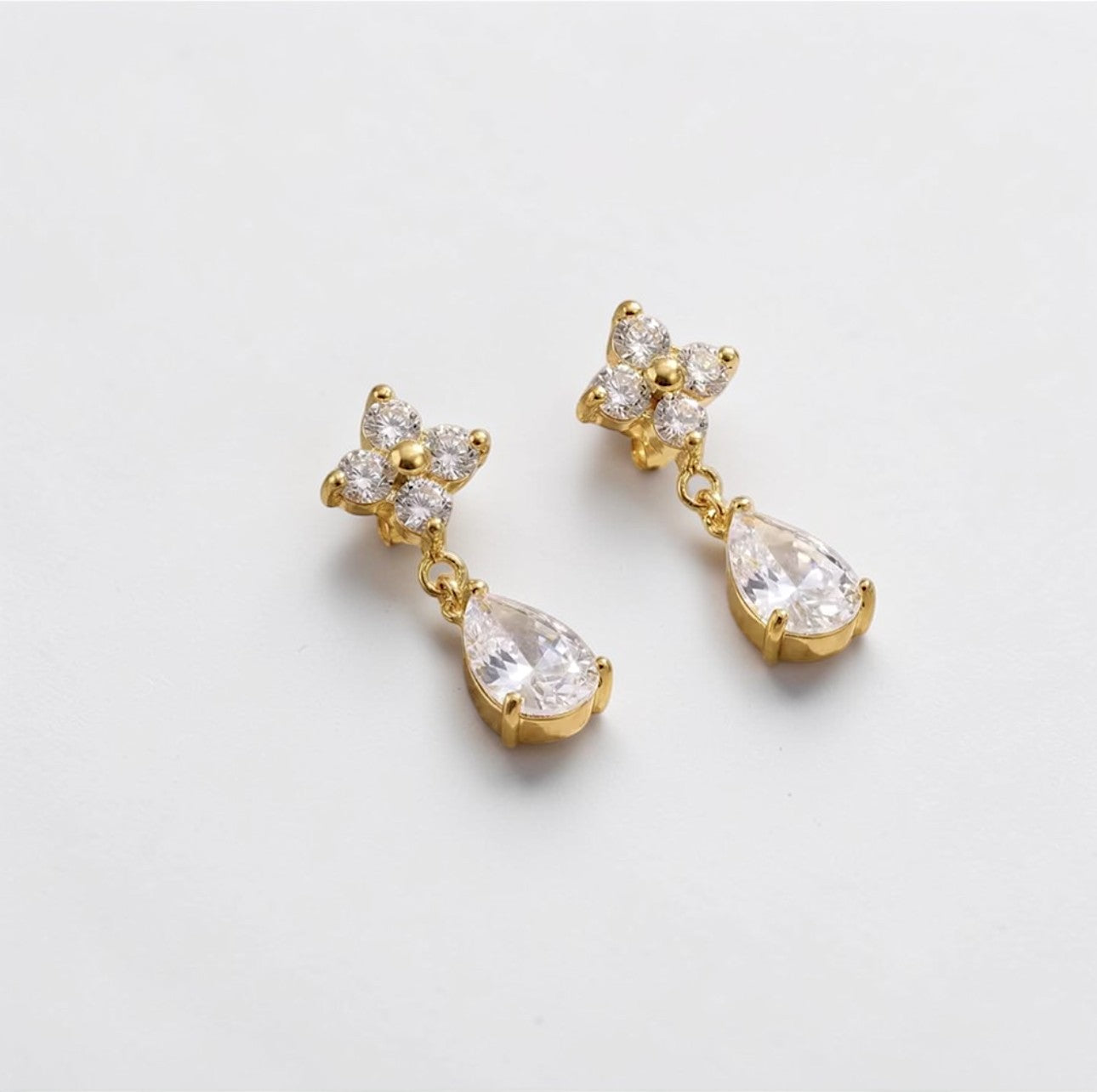 Gold earrings with clear gemstones on a light gray background