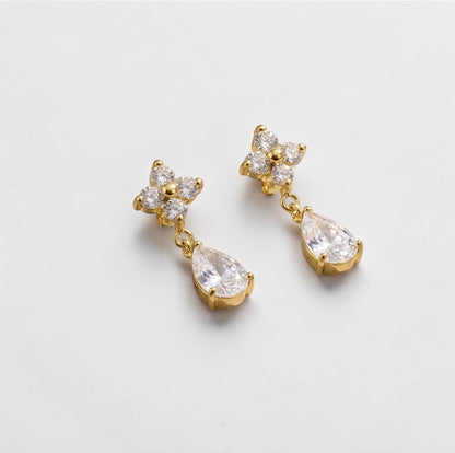 Gold earrings with clear gemstones on a light gray background
