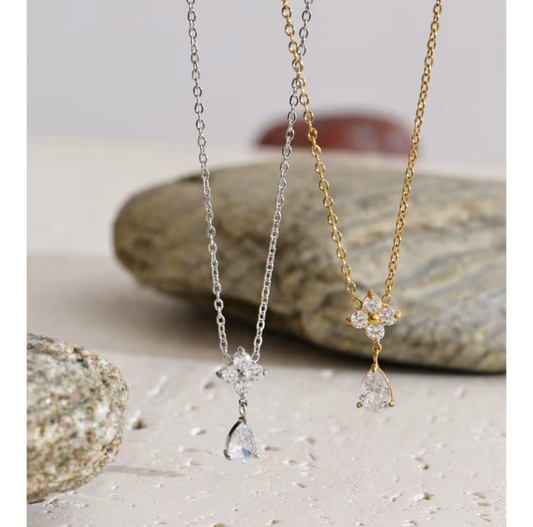 flower shapes gemstone pendant with pear shaped gemstone on a gold necklace pictured on a light grey background