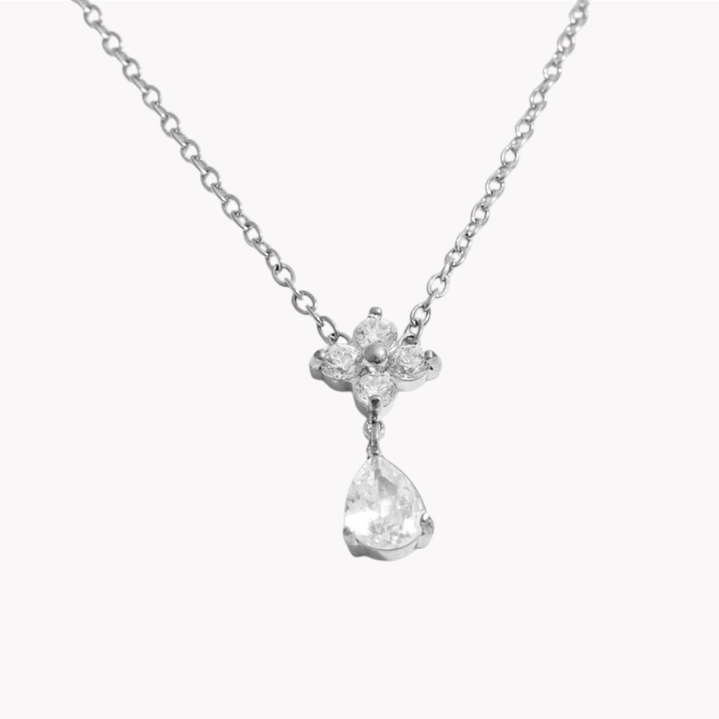 flower shapes gemstone pendant with pear shaped gemstone on a silver necklace pictured on a light grey background