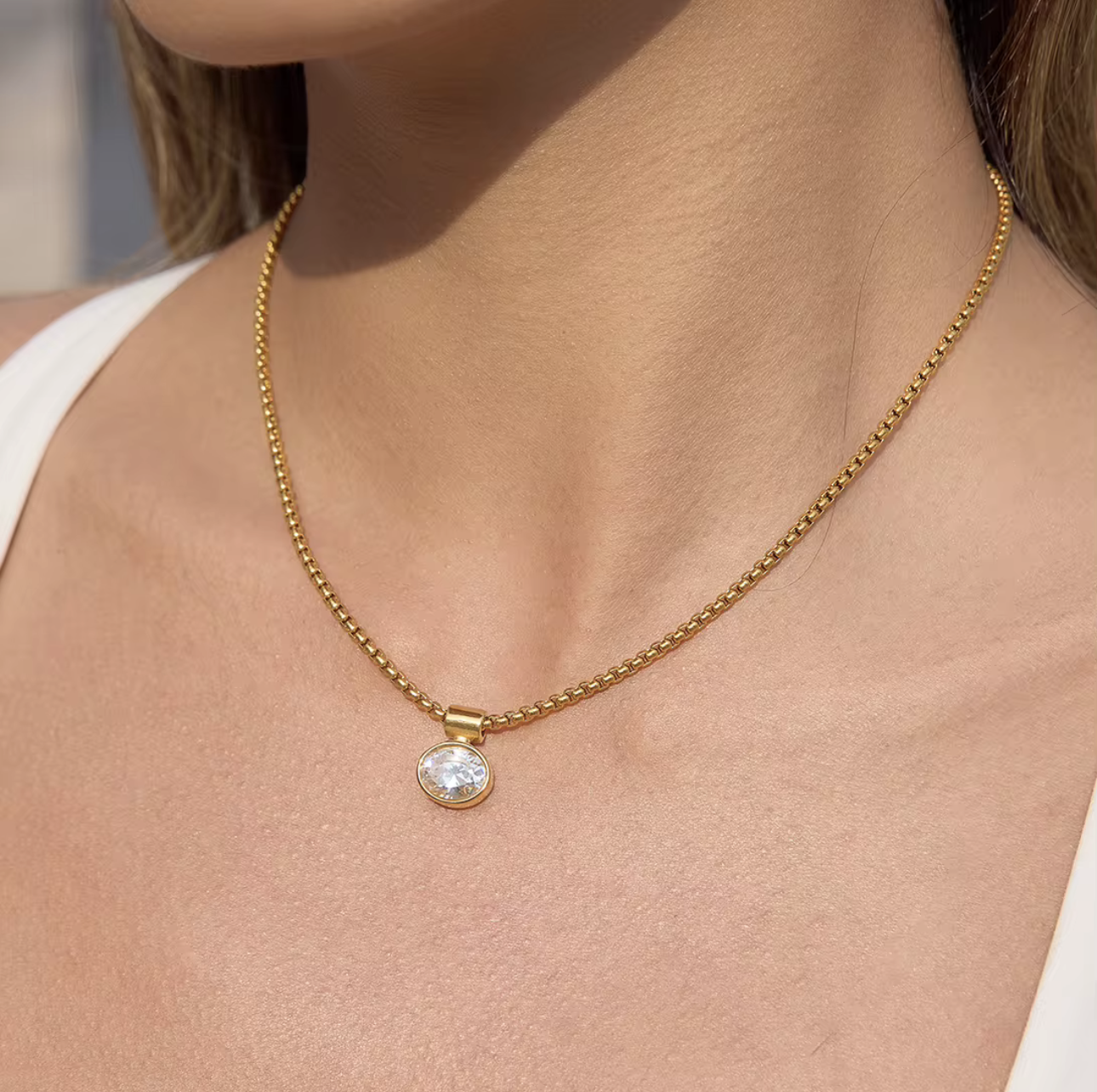 Gold necklace with a pendant on a person wearing a white top.