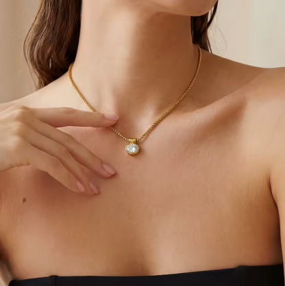 Woman wearing a gold necklace with a diamond pendant, touching her chest.
