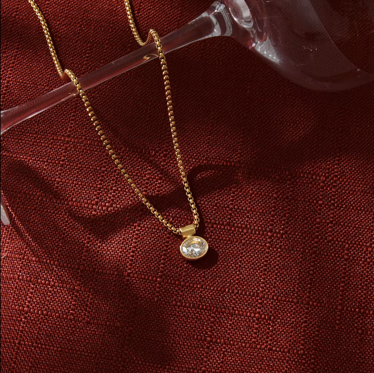 Gold necklace with a diamond pendant on a red fabric background