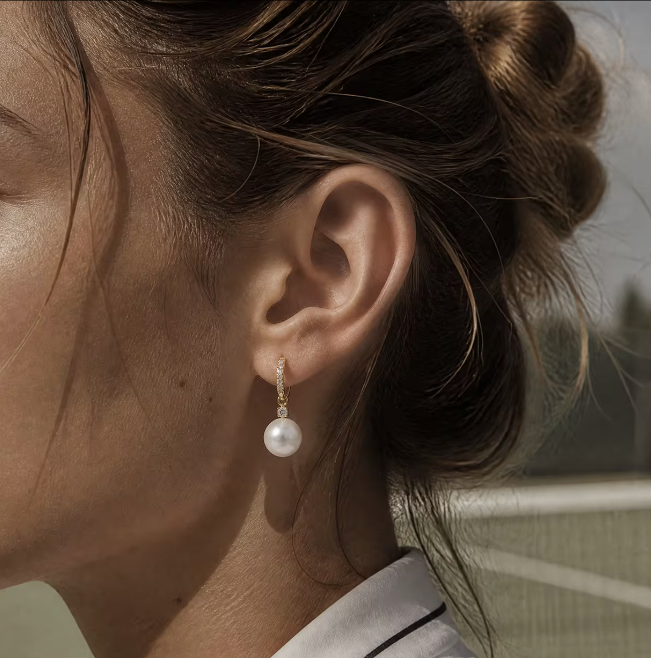 A close-up side profile of a woman wearing a single drop earring with a white pearl and a small gold-toned setting.